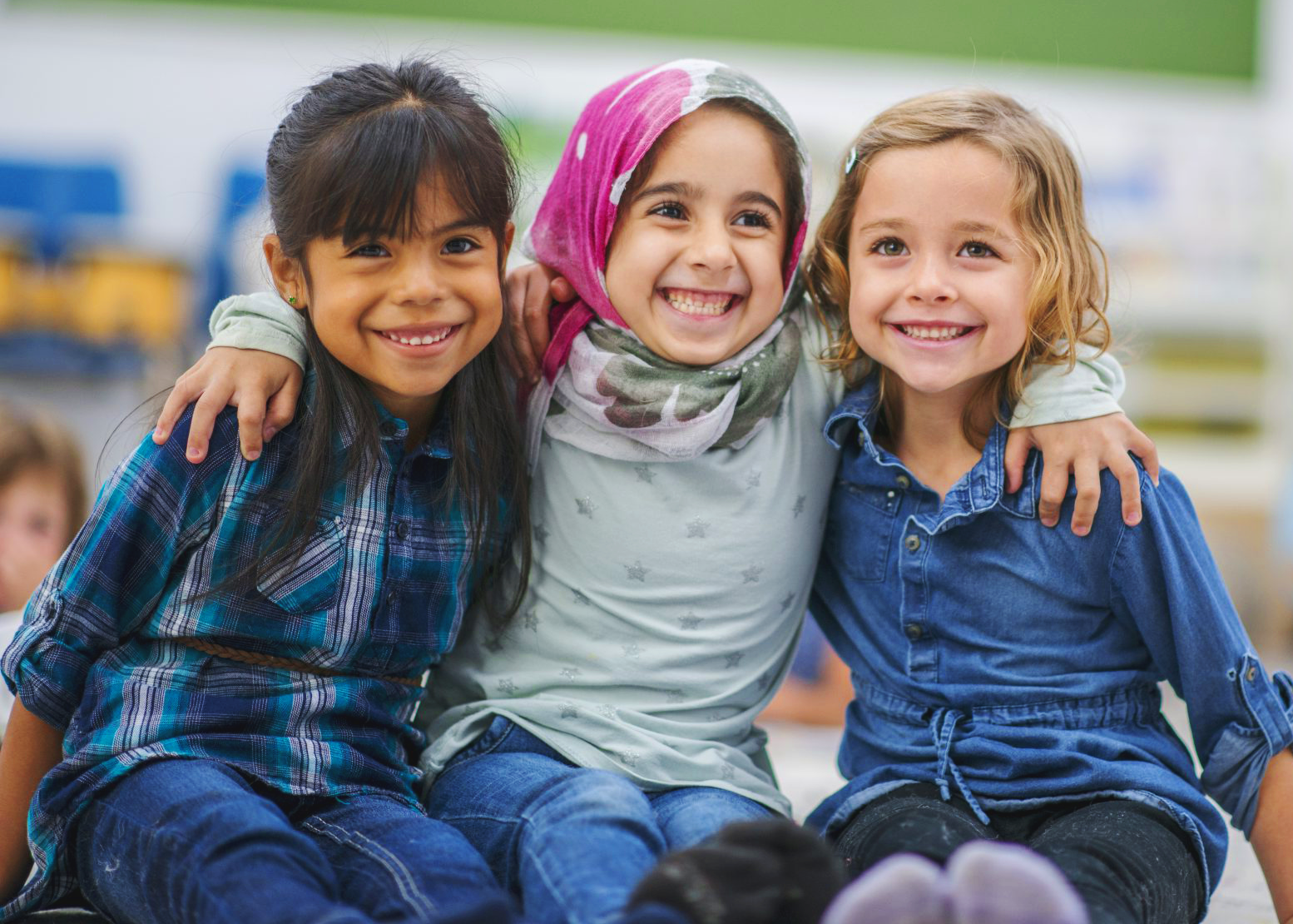 Three elementary school aged children of diverse ethnicities hugging each other